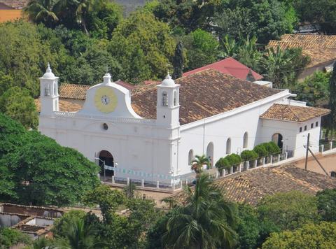 Iglesia blanca de estilo colonial con techo de teja entre árboles